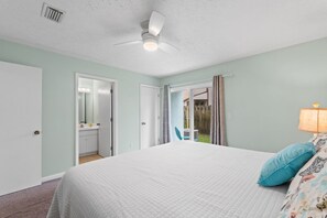 Ein Schlafzimmer mit Bett, Deckenventilator, Badezimmer mit Spiegel und Blick nach draußen.