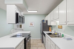 A compact kitchen with white cabinetry, a microwave, a refrigerator, and a sink. - Sleeps 4 2 Bedroom Beach Access Across Street Pool (PANAMA CITY BEACH)