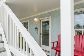 A porch with a white railing, a red chair, and a door with a number sign. - Sleeps 4 2 Bedroom Beach Access Across Street Pool (PANAMA CITY BEACH)
