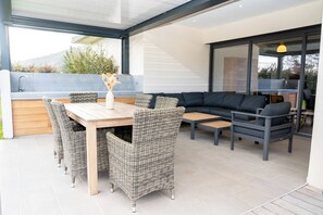 Eine Terrasse im Freien mit einem Holztisch, Korbstühlen, einer schwarzen Couch und einer integrierten Küchenzeile.