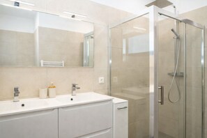 Une salle de bain moderne avec une douche à l’italienne en verre, un meuble-lavabo blanc doté de deux vasques et un grand miroir.