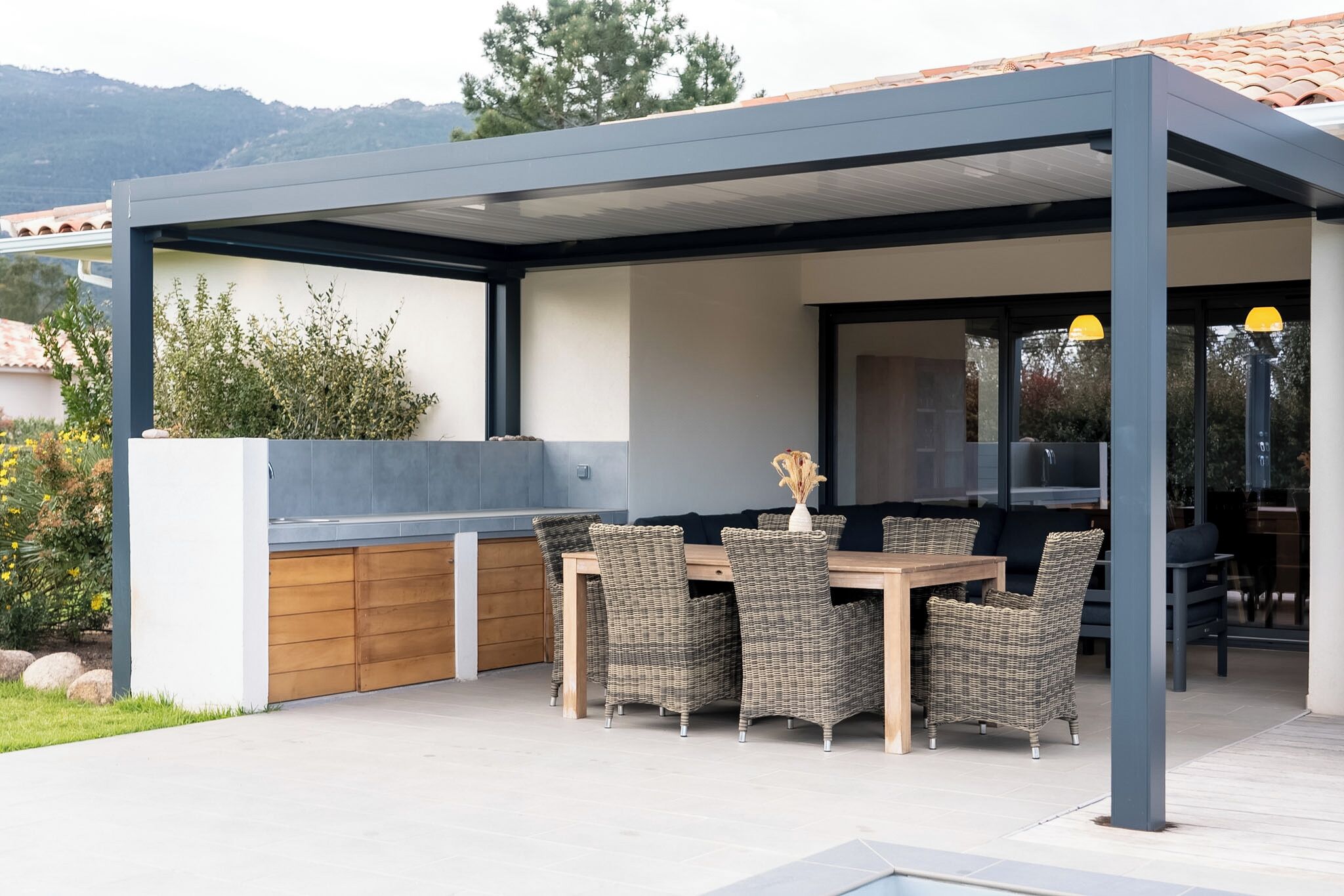 An outdoor patio with a covered dining area, wicker chairs, and a wooden table.