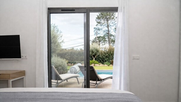 Une chambre avec un lit, une télévision, un bureau et une porte-fenêtre coulissante donnant sur une zone avec piscine.