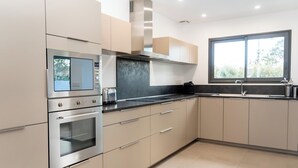 Une cuisine moderne dotée d’appareils électroménagers en acier inoxydable, de meubles de couleur beige et d’une grande fenêtre qui laisse entrer la lumière naturelle.