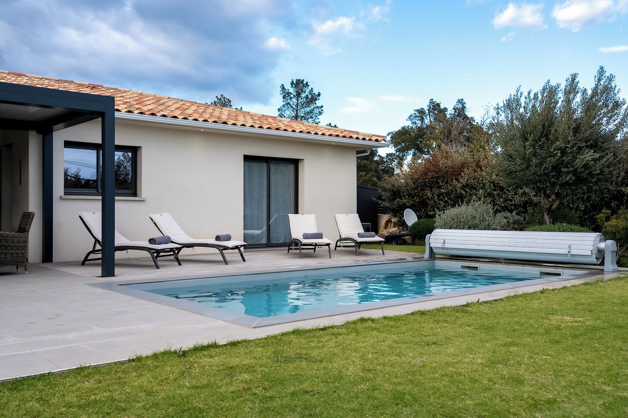 Ein modernes Haus mit Swimmingpool, weißen Liegestühlen und einer überdachten Terrasse.