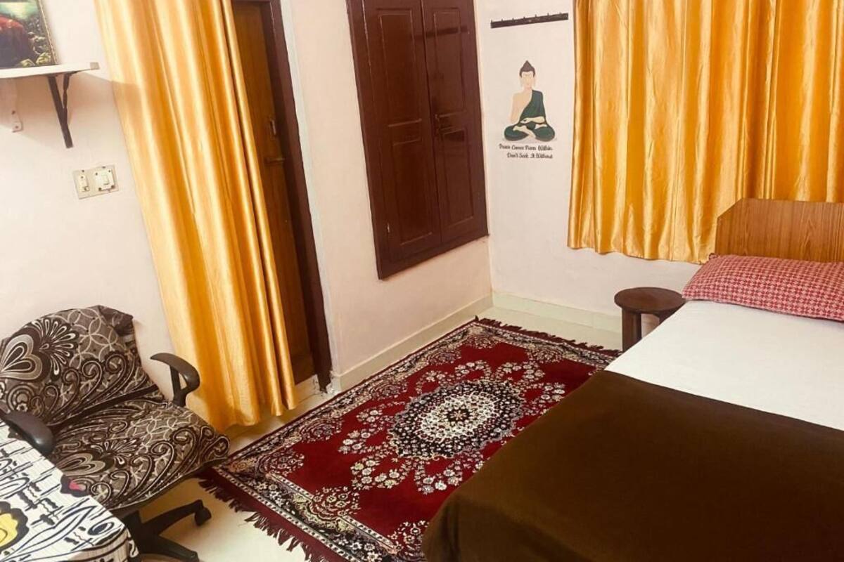 Una habitación con cama, una silla, una puerta y un estante fijado a la pared.