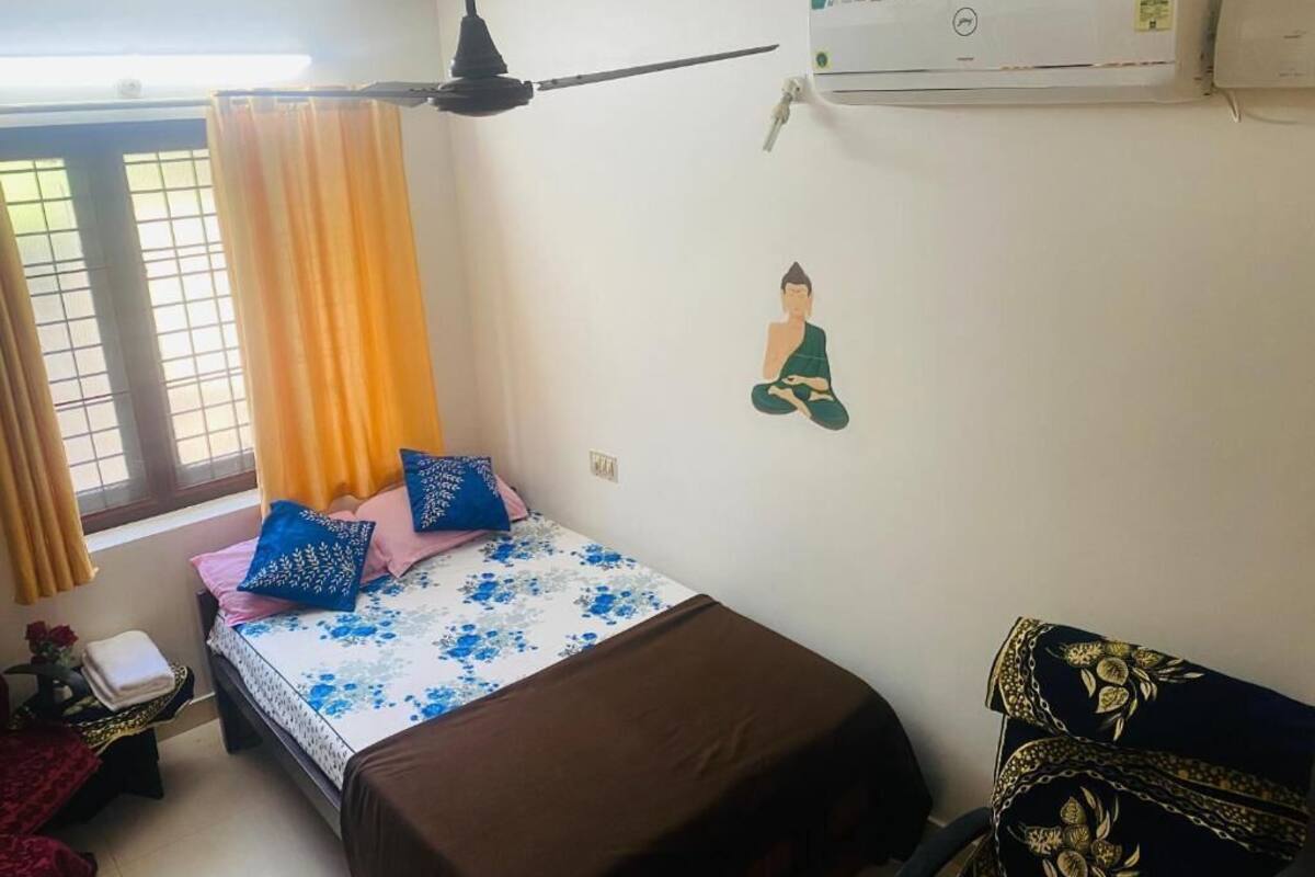 Un dormitorio con cama, aire acondicionado, ventana con cortinas y un adorno en la pared.