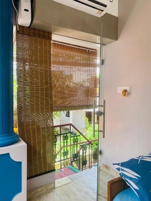 A room with a glass door leading to a balcony, a blue sofa, and a small table. - Homestay - Heaven Aumgarden (Thiruvananthapuram)