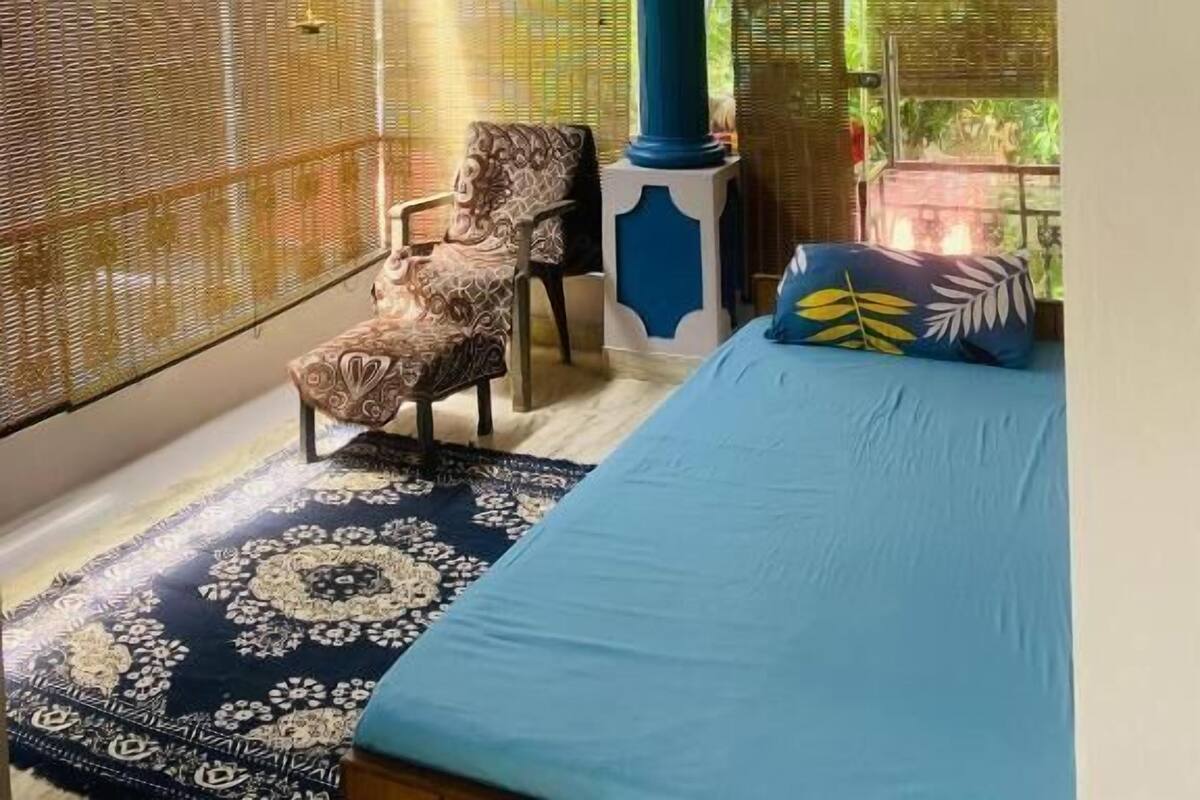 Una habitación con cama, una silla, ventilador de techo, aire acondicionado y ventana con vistas a zonas verdes.