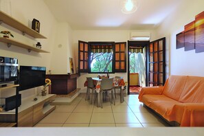 A living room with a TV, sofa, dining table, chairs, and a window with curtains. - Little House Nereids! Seafront vacation! (Quartu Sant'Elena)