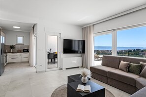 Eine moderne Wohnung mit Küche, Essbereich, Wohnzimmer mit großem Fernseher und einem Balkon mit Blick auf die Stadt.