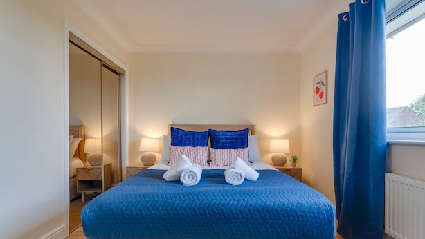 Une chambre d’hôtel avec un lit, deux lampes de chevet, une fenêtre avec des rideaux et une porte donnant sur une autre pièce.