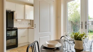 Une cuisine avec des meubles blancs, une cuisinière et un four. On y trouve une table à manger mise avec des assiettes, des verres et une plante.
