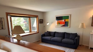 Ein Wohnzimmer mit einer Couch, einer Lampe, einem Gemälde und einem Fenster.