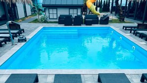 A rectangular swimming pool with clear blue water, surrounded by lounge chairs and a small building in the background. - Air-conditioned holiday homes with swimming pool (Mielno)
