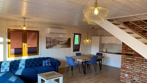 A modern living room with a blue sofa, a dining table with chairs, a small white table, and a staircase leading to an upper level. - Air-conditioned holiday homes with swimming pool (Mielno)