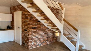 A modern kitchen with white cabinets, a brick accent wall, and a wooden staircase. - Air-conditioned holiday homes with swimming pool (Mielno)
