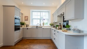 Eine moderne Küche mit weißen Schränken, einem eingebauten Backofen, einem Fenster mit Jalousien und einer Arbeitsplatte mit verschiedenen Küchenutensilien.