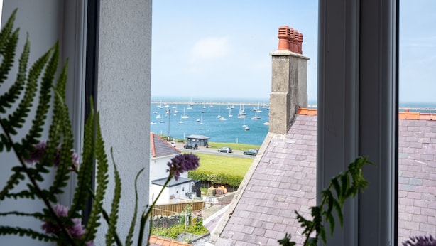 Blick durch ein Fenster auf eine Küstenlandschaft mit Booten, einer Straße und einem Gebäude mit Schornstein.