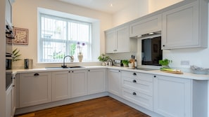 Una cocina moderna con armarios blancos, una ventana con persianas, un fregadero y varios electrodomésticos.