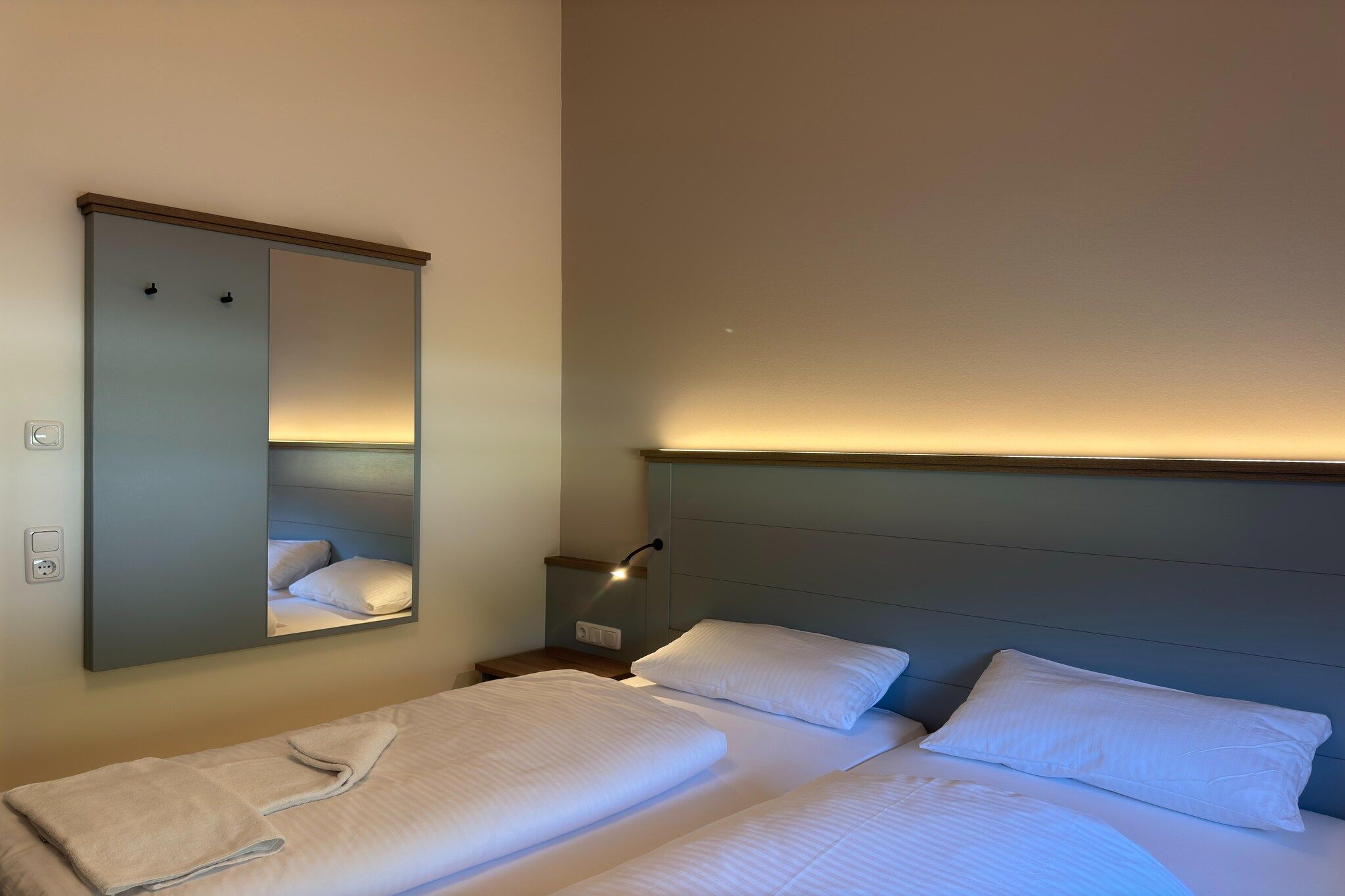 A hotel room with two beds, a nightstand, a mirror, and a wall-mounted light.