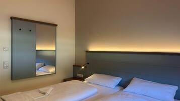 A hotel room with two beds, a nightstand, a mirror, and a wall-mounted light.