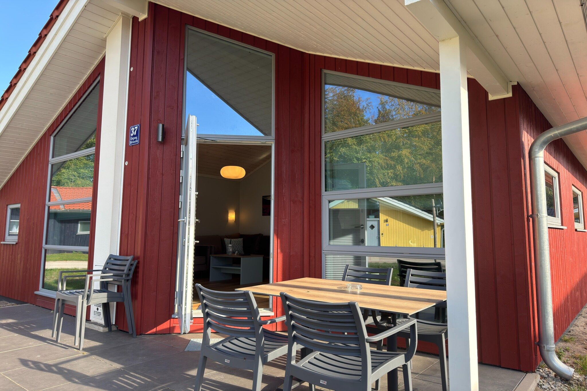 A red building with a table and chairs outside, a door leading inside, and a clear sky.