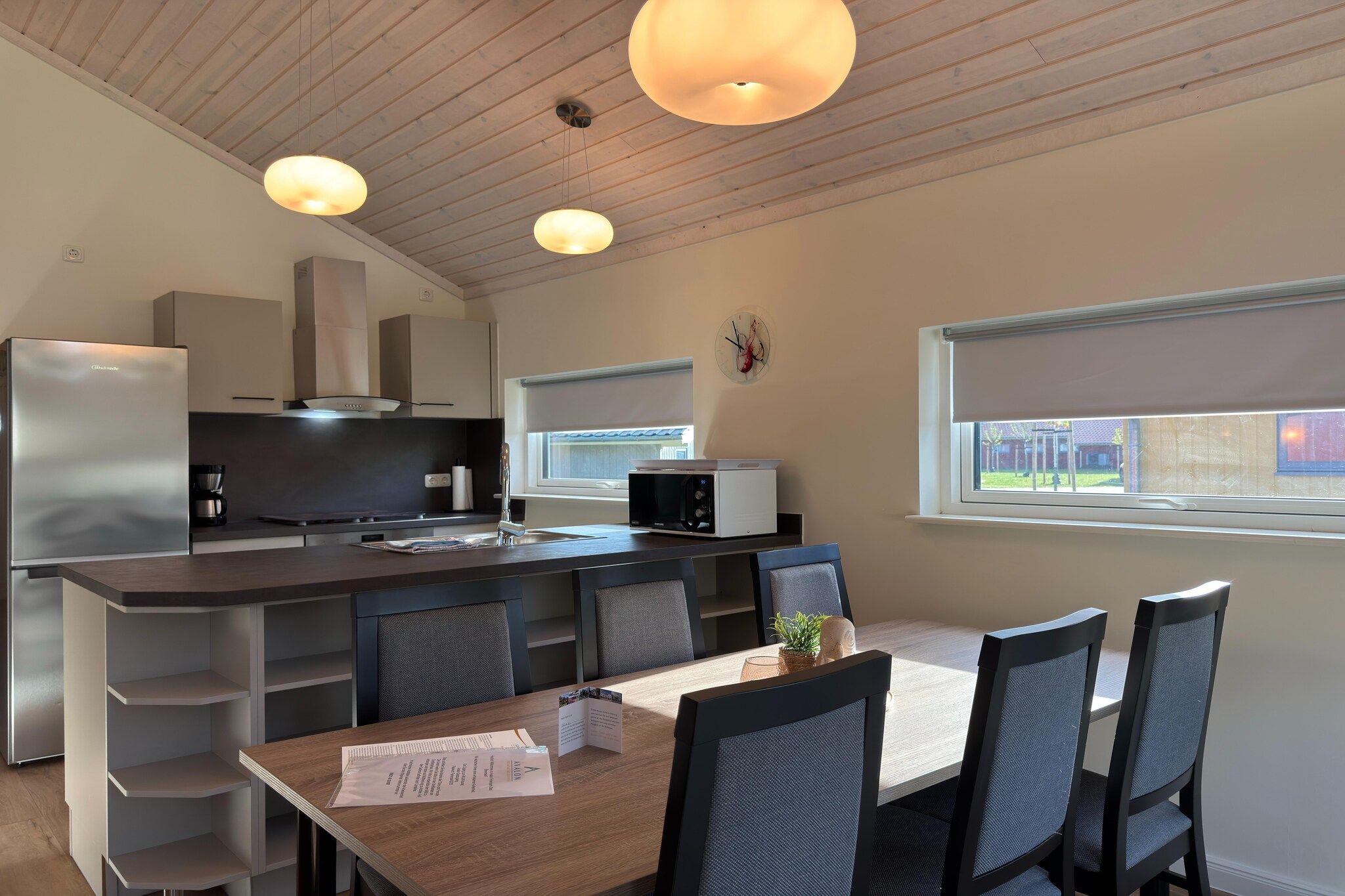 Et moderne køkken med en central ø, et spiseområde med bord og stole, og et vindue med udsigt.