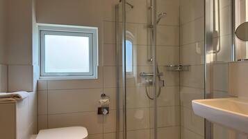 Un baño moderno con ducha envuelta en vidrio, inodoro, lavamanos y ventana que proporciona luz natural.