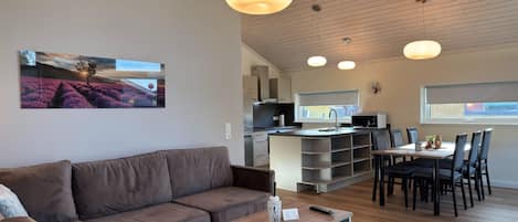 Ein stilvoller Wohnbereich mit Sofa, Couchtisch, Esstisch und Stühlen. Es gibt eine Küchenzeile mit Mikrowelle und Schränken.