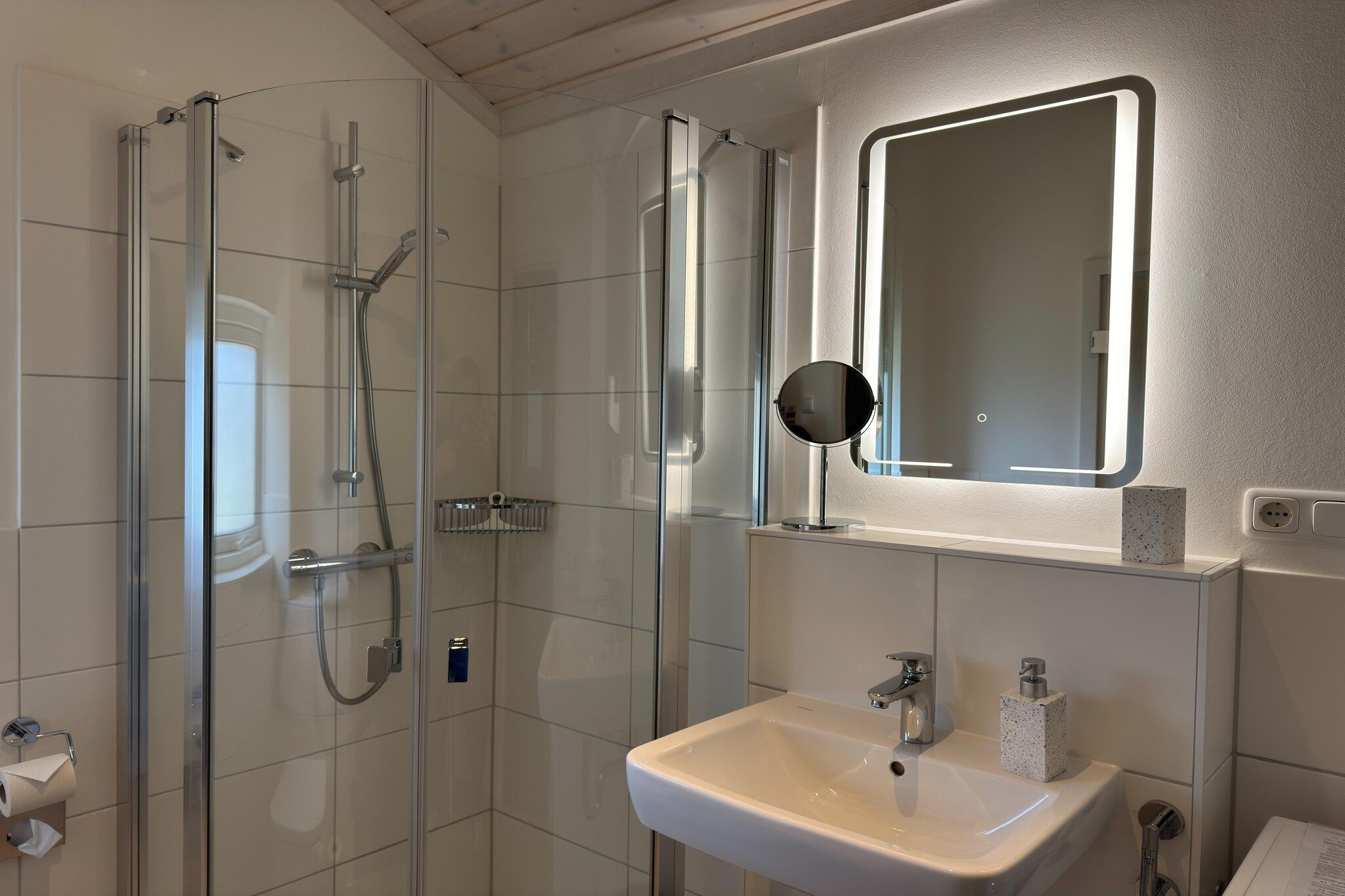 Un baño moderno con ducha de vidrio, un lavamanos con espejo y un inodoro.