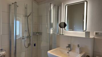 Un baño moderno con ducha de vidrio, un lavamanos con espejo y un inodoro.
