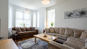 A modern living room with two sofas, a coffee table, and a large window with blinds.