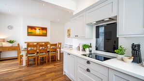 Een moderne keuken met witte kastjes, een eethoek met houten stoelen en een schilderij aan de muur.