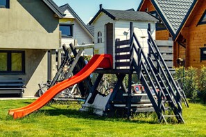 Een speeltuin met een glijbaan en klimconstructie in een woonwijk, met huizen op de achtergrond.