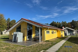 Un edificio amarillo con techo rojo, un área de estar al aire libre cubierta y un letrero que dice 'Haus 36'.