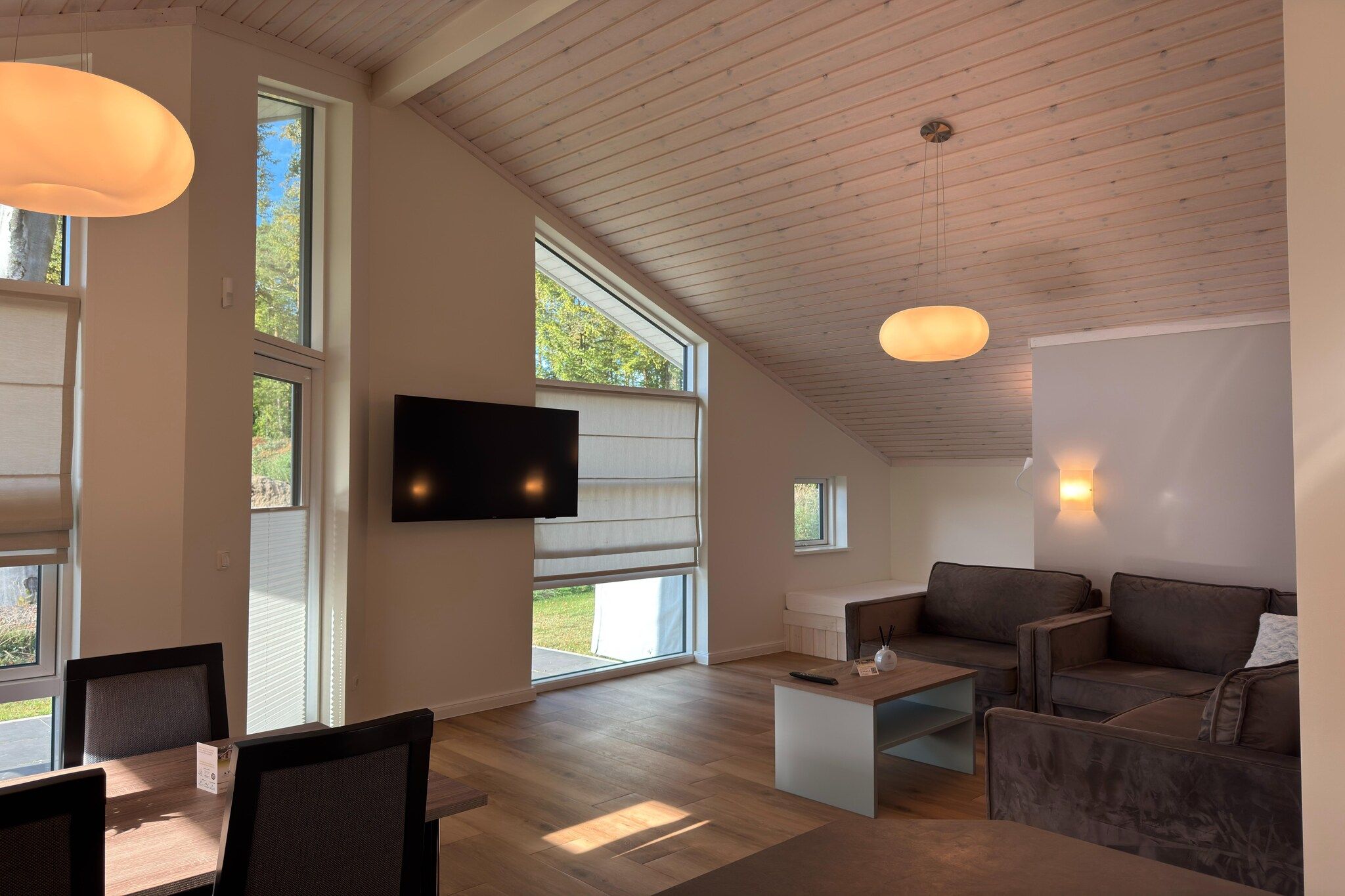 Un vaste espace de vie doté d’un téléviseur à écran plat, d’un plafond en bois, de grandes fenêtres et d’un coin salon confortable.