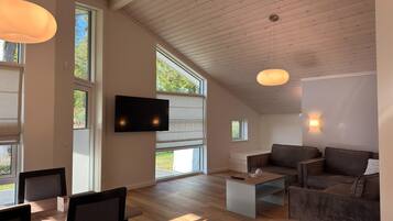 Un vaste espace de vie doté d’un téléviseur à écran plat, d’un plafond en bois, de grandes fenêtres et d’un coin salon confortable.