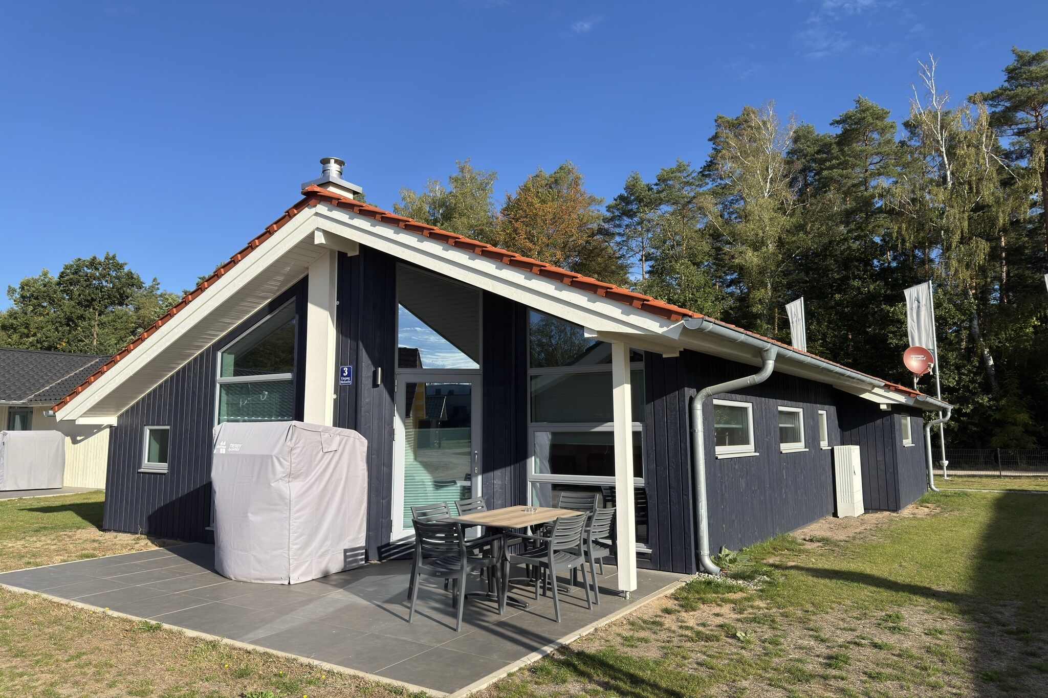 Een klein gebouw met een overdekt terras, een tafel en stoelen.