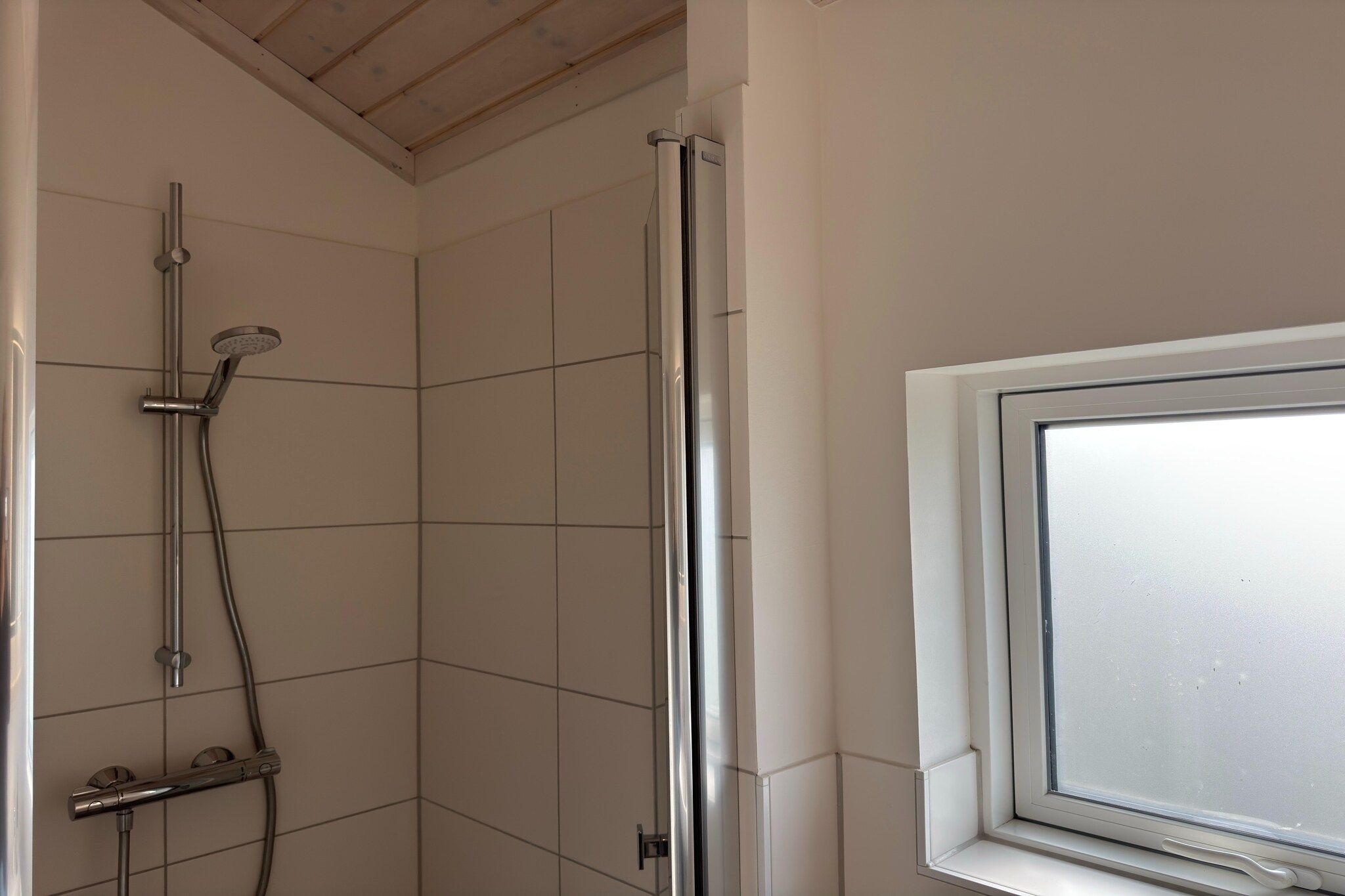 Eine Dusche mit Glastür, ein Fenster mit Milchglas und geflieste Wände.