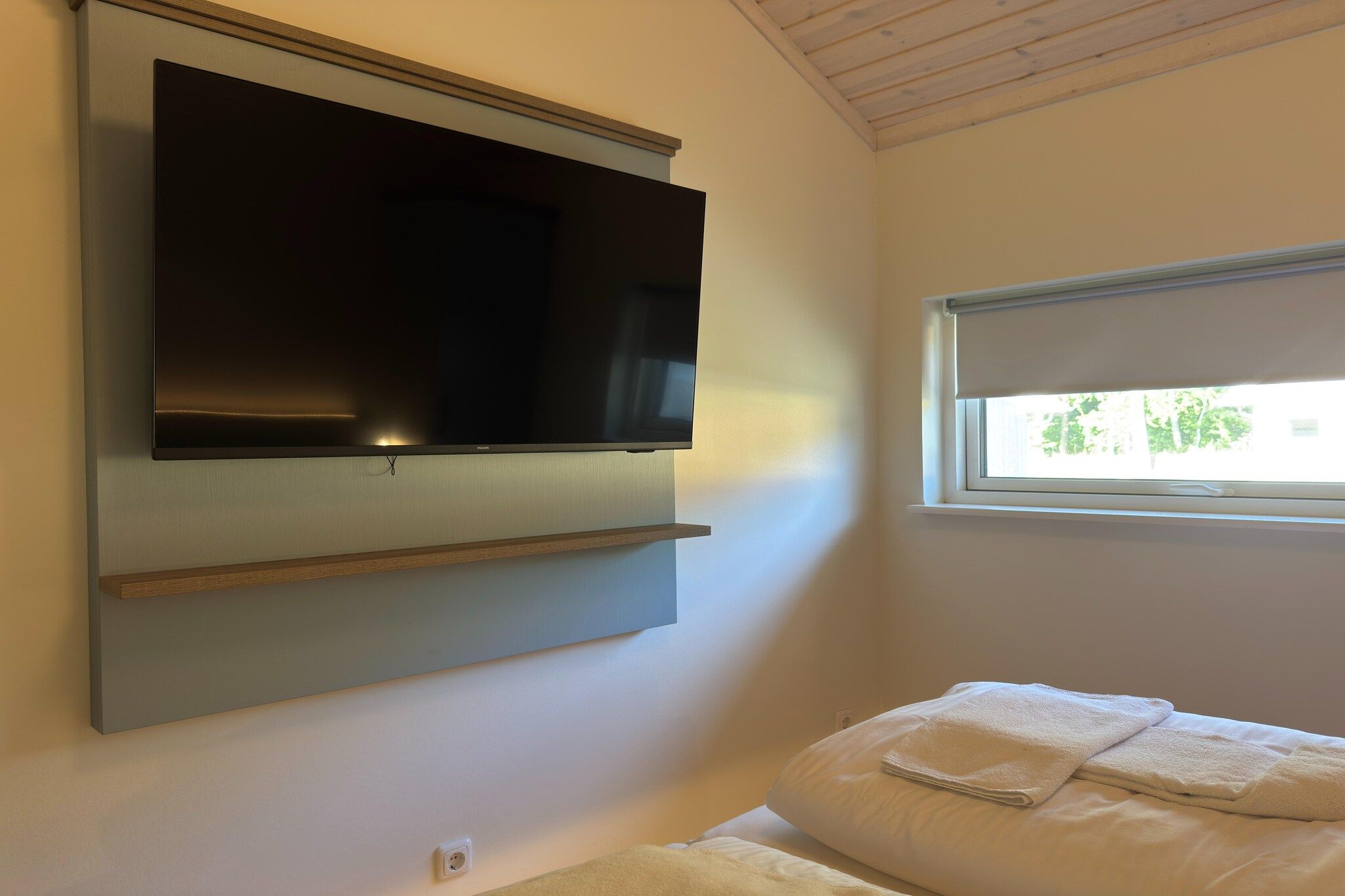 A bedroom with a mounted television, a window with a view, and a bed with pillows.