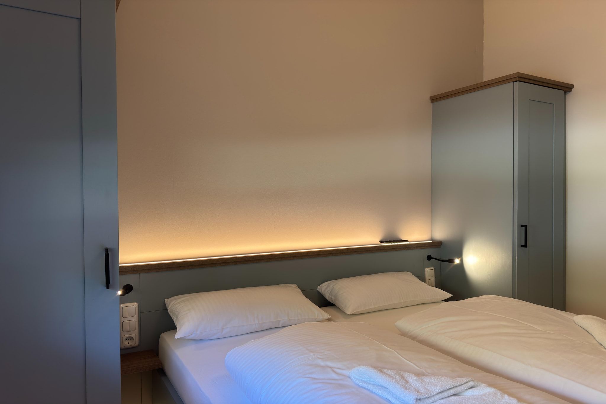 Ett sovrum med en säng, två kuddar, ett sängbord, en lampa och en garderob.