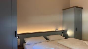A bedroom with a bed, two pillows, a bedside table, a lamp, and a wardrobe.