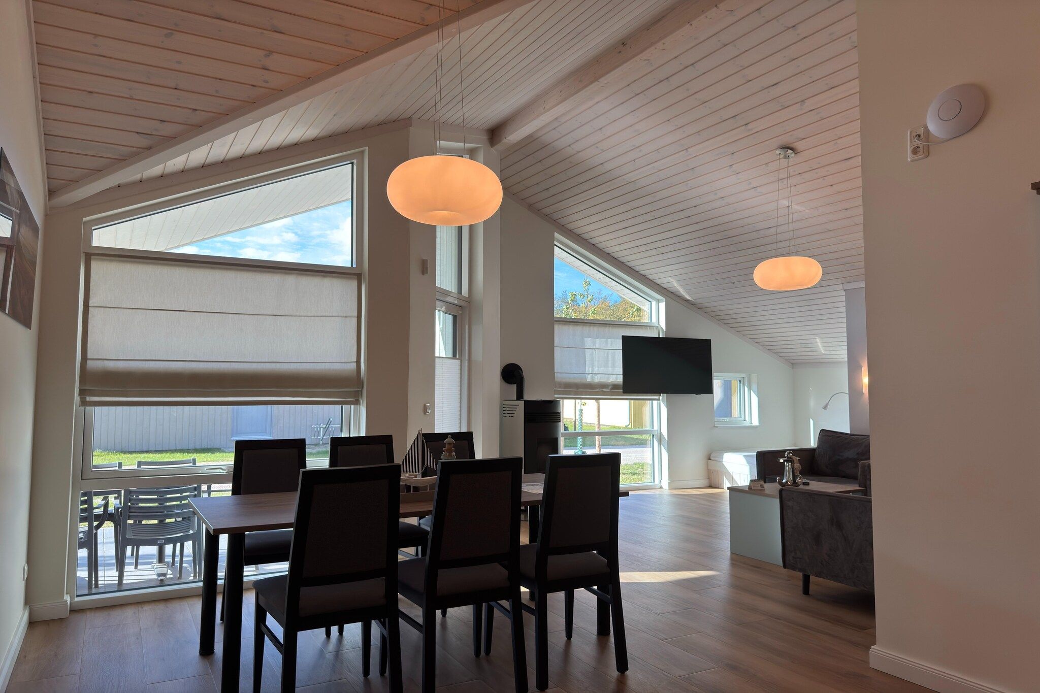 A spacious dining area with a high ceiling and large windows, a television mounted on the wall, and a cozy seating area with a fireplace.