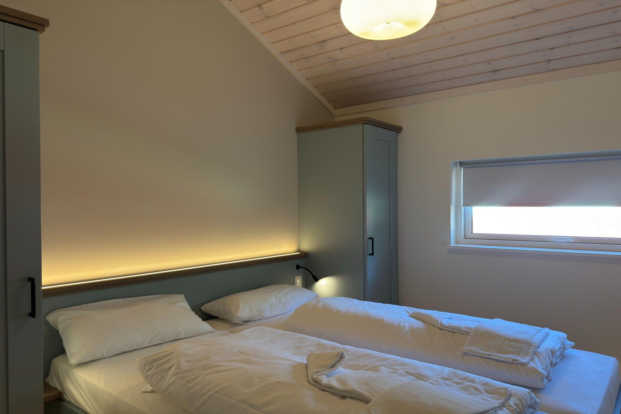 A bedroom with a bed, a bedside lamp, a window, and a wardrobe.