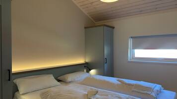 A bedroom with a bed, a bedside lamp, a window, and a wardrobe.