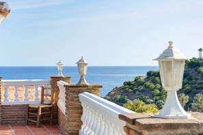 Una terraza con vista al mar, baranda blanca y un farol.