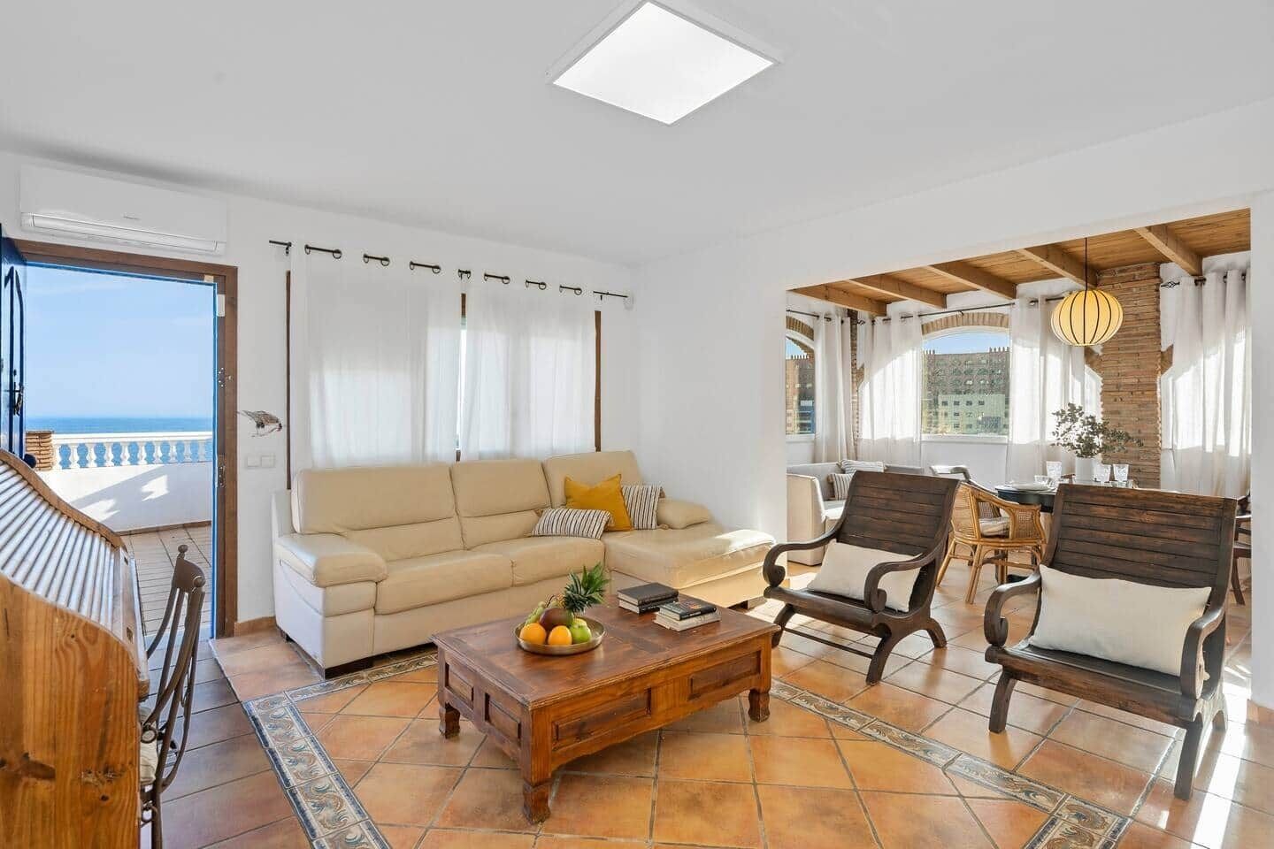 Un soggiorno con divano, tavolino in legno e poltrone, un balcone con vista e un'area pranzo con tavolo e sedie.