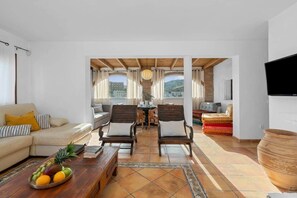 Un salón espacioso con un sofá, dos sillones, una mesa de centro con fruta, un televisor y vistas a la montaña.