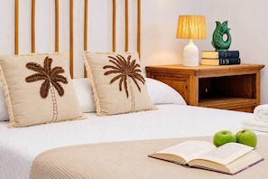 Una cama bien hecha con dos almohadas, una mesita de noche con una lámpara y libros, y un libro abierto sobre la cama.
